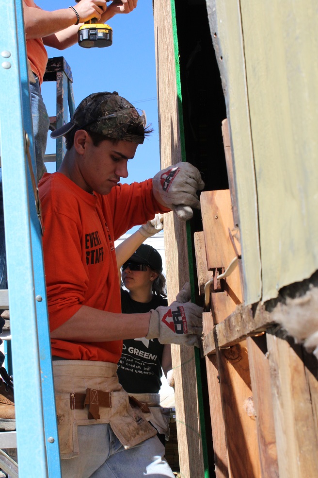 IMAGE: Matthew Chebowski helps replace siding and a window for a mother who just purchased her first home.