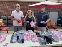Greg Hershberg, Jodie Elliott, and Ben Ridner stand with a table of donated shoes.