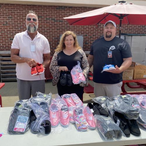 Greg Hershberg, Jodie Elliott, and Ben Ridner stand with a table of donated shoes.