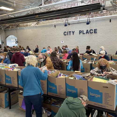 Community members browse tables of boxes for books, food, clothing, and other items delivered through ASTAR’s partnership with Operation Sharing.